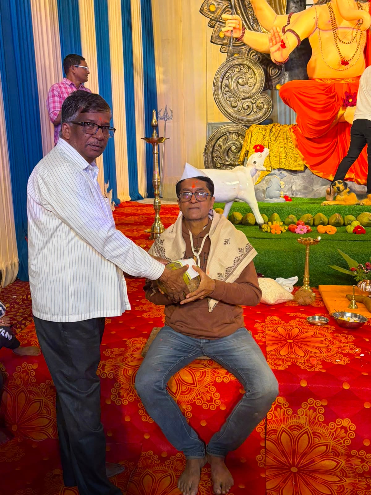 A community elder honoring the idol sculptor with a coconut during the Murtikar felicitation, 2026